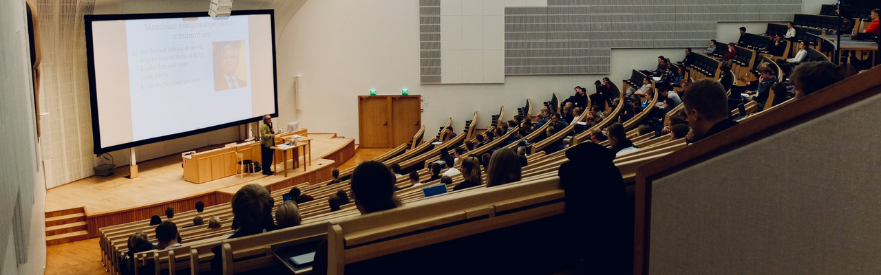 Menschen sitzen in einem Hörsaal und hören einem Vortrag zu. 